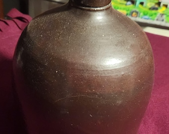 May include: A brown stoneware crock with a wide mouth and a rounded body. The crock has a simple, rustic design and is glazed in a dark brown color.