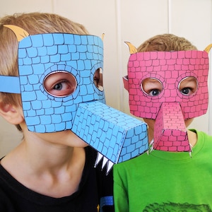 Könnte beinhalten: Zwei Kinder tragen Papierdrachenmasken. Die Maske links ist blau und die Maske rechts ist rosa. Beide Masken haben ein Ziegelmuster.