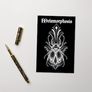 Puede incluir: Una impresión artística en blanco y negro con una ilustración detallada de un escarabajo y la palabra "Metamorphosis". También hay dos bolígrafos decorativos con diseños florales dorados y negros.