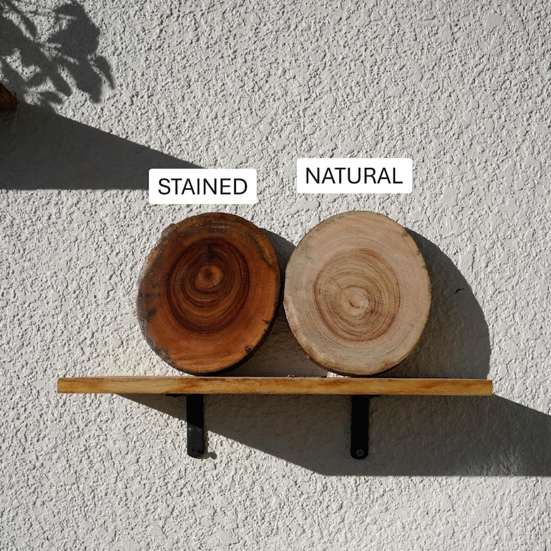 K&ouml;nnte beinhalten: Zwei Holzscheiben, eine gebeizt und eine nat&uuml;rlich, auf einem Holzregal mit schwarzen Metallhalterungen. Die gebeizte Scheibe ist ein sattes Braun, w&auml;hrend die nat&uuml;rliche Scheibe hellbraun ist. Die W&ouml;rter "STAINED" und "NATURAL" sind aufgedruckt.