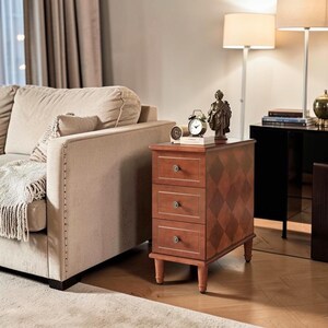 May include: A wooden end table with three drawers, each featuring a single round knob. The side panel displays a brown diamond pattern. The table stands on four short legs and is topped with a small analog clock and a decorative figurine.