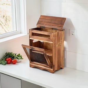 May include: A wooden kitchen storage cabinet with a hinged lid and a door that is ajar. The cabinet is made of light brown wood and has a mesh screen on the door. The cabinet is sitting on a white countertop.