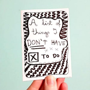 Può includere: Una carta bianca con testo nero scritto a mano che recita "A list of things I DON'T HAVE TO DO". La carta è tenuta in mano e ha un bordo decorativo con un disegno ondulato. Lo sfondo è di colore azzurro.