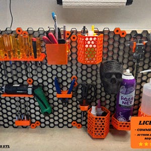 Puede incluir: Un organizador de pared modular negro y naranja con varias herramientas y accesorios. El organizador presenta un diseño de panal con soportes y soportes naranjas para destornilladores, bolígrafos, tijeras y otros artículos. También se ve una calavera y un pulverizador.