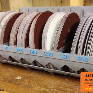 May include: A gray, 3D-printed sanding disc organizer filled with various grit sandpaper discs. The organizer has blue numbers indicating grit sizes: 40, 60, 80, 120, 180, 240, 320, and 400. The discs are brown and beige.