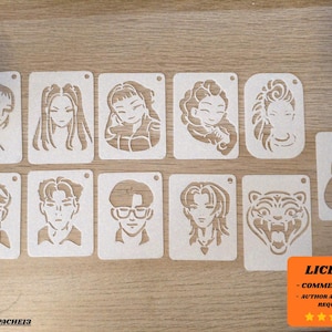 Può includere: Una collezione di stencil in legno con vari ritratti stilizzati di persone e una tigre. Ogni stencil è rettangolare con un piccolo foro nella parte superiore. Gli stencil sono disposti su una superficie di legno marrone chiaro. L'immagine include un avviso di licenza.