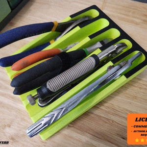 Puede incluir: Un organizador de herramientas verde lima y negro que contiene varias herramientas manuales. Las herramientas incluyen alicates con mangos azules, herramientas con mango naranja y otras herramientas metálicas. El organizador está sobre una superficie de madera.