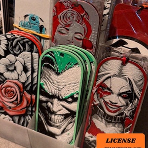 May include: A display of various character-themed bookmarks. The bookmarks feature images of the Joker, Harley Quinn, and other pop culture characters. The bookmarks are in clear plastic packaging and are displayed in a cardboard container. The image includes the text "LICENSE - COMMERCIAL USE - AUTHOR ATTRIBUTION REQUIRED".