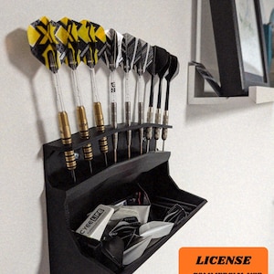 May include: A black dart holder with several darts and extra flights. The darts have yellow and black, black and white, and solid black flights. The holder has a storage area for extra dart flights and accessories.