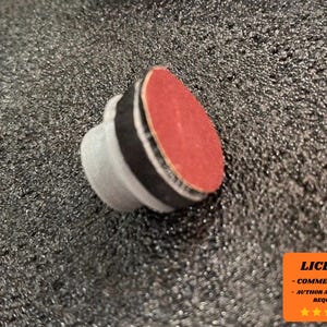 May include: A small, gray object with a red, circular top and a black band. The object is set against a textured, dark gray background. The image also includes an orange square with white text indicating a license for commercial use.