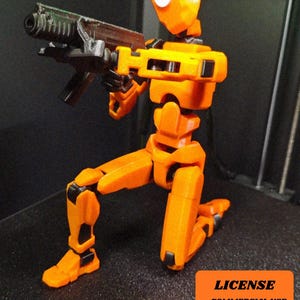 May include: An orange and black articulated robot figure, kneeling and holding a black and brown gun. The robot has a unique design with visible joints and a distinct head shape. The figure is on a black surface.