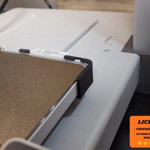 Könnte beinhalten: Nahaufnahme eines rechteckigen Geräts mit einer strukturierten braunen Oberfläche und schwarzen Eckschützern. Ein weißes Etikett mit Text ist sichtbar. Das Gerät befindet sich auf einer weißen Oberfläche. Ein orangefarbenes Quadrat mit Text und Sternen befindet sich in der unteren rechten Ecke.