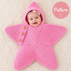 May include: A bright pink crocheted star-shaped baby bunting with a hood and three light brown wooden buttons along the side. The garment features a textured stitch pattern and a small pink bow headband. The image includes the text Pattern.