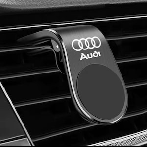 Puede incluir: Soporte negro para teléfono de ventilación de coche con el logotipo de Audi en blanco. El soporte tiene una superficie magnética para sujetar el teléfono y una pinza para fijarlo. Fabricado en metal.