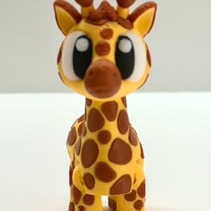 Puede incluir: Una figura de jirafa amarilla con manchas marrones y ojos grandes y expresivos. La jirafa tiene un diseño amigable y de dibujos animados, con pequeños cuernos marrones y un patrón detallado. La figura está de pie, mostrando sus distintivas marcas.