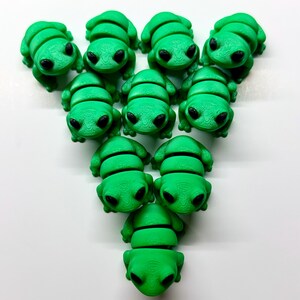 Pode incluir: Uma cole&ccedil;&atilde;o de onze figuras de sapos verdes brilhantes com olhos pretos. Os sapos est&atilde;o dispostos em um padr&atilde;o triangular sobre um fundo branco. Cada sapo tem um corpo segmentado e uma cabe&ccedil;a lisa e arredondada.