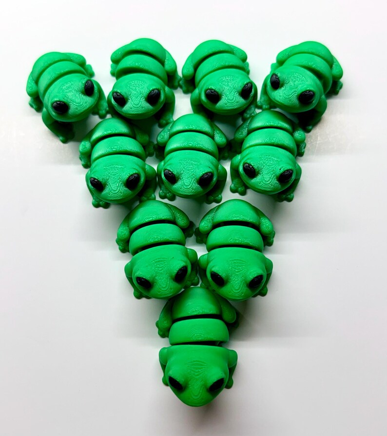 Pode incluir: Uma cole&ccedil;&atilde;o de onze figuras de sapos verdes brilhantes com olhos pretos. Os sapos est&atilde;o dispostos em um padr&atilde;o triangular sobre um fundo branco. Cada sapo tem um corpo segmentado e uma cabe&ccedil;a lisa e arredondada.