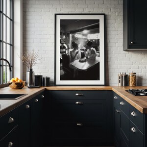 Vintage diner women pie poster framed in white mat black frame on white painted brick wall above black kitchen cabinets with wood countertop and modern appliances