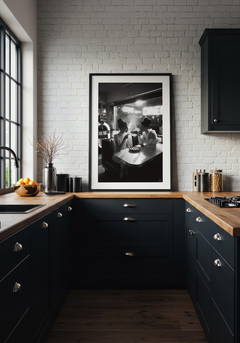 Vintage diner women pie poster framed in white mat black frame on white painted brick wall above black kitchen cabinets with wood countertop and modern appliances