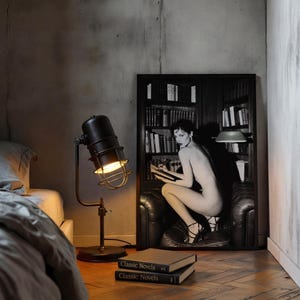 Może przedstawiać: Czarna lampa biurkowa w stylu industrialnym z kloszem w kształcie klatki oświetla pok&oacute;j z czarno-białą oprawioną grafiką kobiety czytającej. Dwie książki zatytułowane "Classic Novels" są ułożone na podłodze.