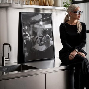 Retro diner ladies poster displayed in modern stainless steel kitchen with woman in sunglasses gold glassware and contemporary design showing black white photography
