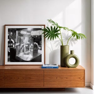 Vintage women diner photo poster in wood frame displayed on mid-century walnut credenza with green ceramic vases tropical plants and architecture books contemporary interior