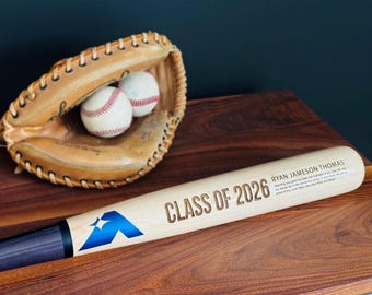 以下が含まれることがあります： 青いロゴ、「CLASS OF 2026」の文字、そして「RYAN JAMESON THOMAS」という名前が刻印された明るい色の木製野球バット。赤い縫い目の白い野球ボール2個が入った、日焼けした革製の野球グローブが添えられています。