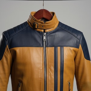May include: A tan and navy blue leather jacket on a wooden hanger. The jacket has a zip-up front, a stand-up collar with a buckle, and navy blue stripes. The shoulders have quilted detailing. The jacket is a classic design.
