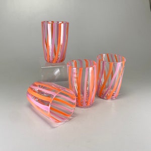 Puede incluir: Cuatro vasos de vidrio transparente con diseños de rayas rosas y naranjas. Los vasos están apilados uno encima del otro.
