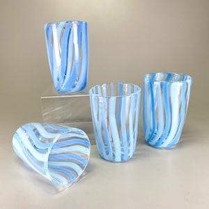 Puede incluir: Cuatro vasos de vidrio transparente con diseños de rayas azules y blancas. Los vasos están dispuestos en forma escalonada sobre una superficie blanca.