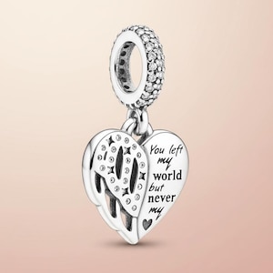 May include: Silver charm with a heart-shaped pendant. The pendant has a cut-out design and the inscription "You left my world but never my". The charm's ring is encrusted with small, clear stones.