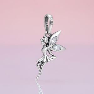 May include: A silver fairy charm pendant with a loop for a necklace. The fairy has detailed wings with clear, sparkling accents. The pendant is made of silver and has the text "S925" on the loop.