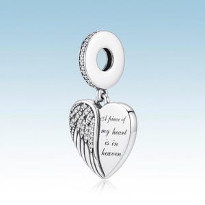 May include: Silver charm with a heart and wing design. The heart-shaped pendant has the inscription "A piece of my heart is in heaven." The charm features a ring at the top, embellished with small, sparkling stones. The wing is detailed with small, sparkling stones.
