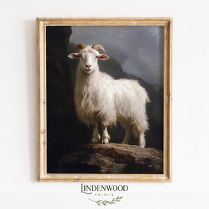 May include: A framed print of a white goat with long, shaggy fur, standing on a rocky outcrop. The goat has curved horns and is set against a dark, moody landscape. The frame is a light gold color, and the print has the text "LINDENWOOD PRINTS" at the bottom.