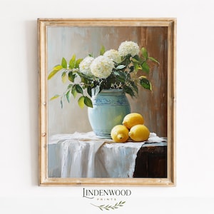 May include: A framed still life painting featuring a light blue vase with white flowers and green leaves. Three yellow lemons rest on a white tablecloth. The painting has a gold frame and a vintage aesthetic.