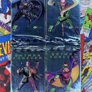 Puede incluir: Cuatro paquetes sellados de cromos "Batman Forever". Cada paquete presenta un personaje diferente: Batman, Enigma, Dos Caras y Robin. Los paquetes son plateados metálicos con el logo "Batman Forever" y "6 Cartas" impresas.
