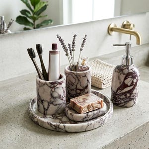 May include: A marble bathroom set featuring a soap dispenser, toothbrush holder, and tray. The set includes a soap dish with a bar of soap, a small vase with lavender, and a tube of toothpaste. The marble has a white and burgundy pattern.