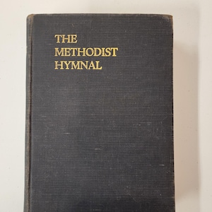 May include: A vintage, dark blue book titled "THE METHODIST HYMNAL" in gold lettering. The book has a textured cover and shows signs of wear, suggesting its age. The title is centered on the cover.