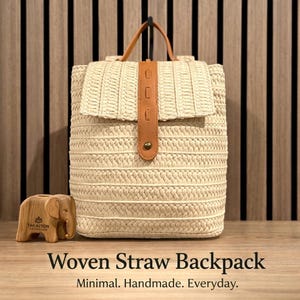 May include: A cream-coloured woven straw backpack with a flap closure and a brown leather strap. The bag has a top handle and a brown leather strap closure with a button. The text "Woven Straw Backpack" is at the bottom.