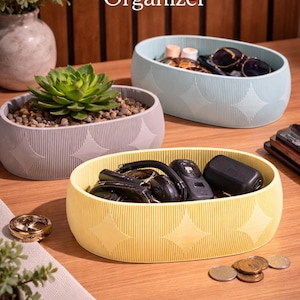 Puede incluir: Una taza de cerámica blanca con un asa negra y el texto "But First, Coffee" en un estilo manuscrito. La taza está sobre una superficie blanca. La taza mide aproximadamente 10 cm de alto.