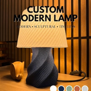 May include: A custom modern lamp with a woven lampshade and a dark blue, twisted base. The image text reads "CUSTOM MODERN LAMP" and "MODERN • SCULPTURAL • TIMELESS". Multiple colours are available.