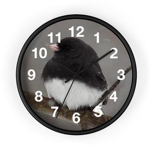 May include: Black and white bird wall clock with a black frame. The clock face features a detailed image of a bird perched on a branch, with white numerals marking the hours. The clock measures approximately 10 inches in diameter.