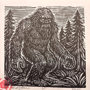 May include: Black and white linocut print of Bigfoot, also known as Sasquatch, in a forest setting. The artwork features the creature with long, shaggy hair, surrounded by trees and foliage. The print is signed and dated.
