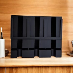 May include: A black organizer with multiple compartments, designed for kitchen or office use. The organizer has a rectangular shape with vertical slots and lower cubby spaces. It is placed on a wooden surface.