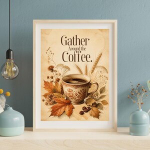 Può includere: Una stampa artistica incorniciata con una tazza di caffè circondata da foglie autunnali, spighe di grano e fiori secchi su sfondo beige. Il testo Gather Around the Coffee è stampato in lettere marrone scuro sopra la tazza con chicchi.