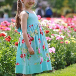 May include: A young girl wearing a light blue dress with a floral print and white polka dots. The dress has a gathered skirt and a fitted bodice. The girl is standing in a field of flowers.