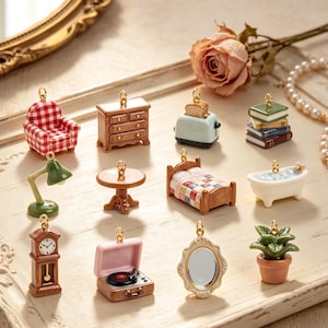 May include: A collection of twelve miniature charms featuring household items including a red and white chequered armchair, a brown wooden dresser, a blue toaster with toast, a stack of books, a green desk lamp, a round table, a bed, a bathtub, a grandfather clock, a record player, a mirror, and a potted plant.