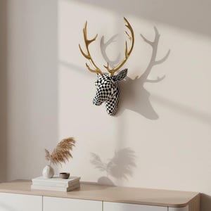 May include: A decorative deer head wall mount. The head is black and white checkered, with gold-coloured antlers. The deer head is mounted on a light-coloured wall, casting a shadow. The overall theme is home decor.