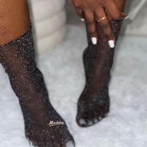 Peut inclure: Bas noirs transparents avec des embellissements scintillants. Les bas sont portés sur les pieds et le bas des jambes. Le texte "Missluna" est visible en bas à gauche de l'image.