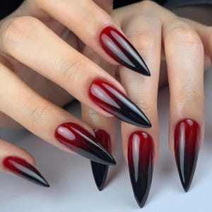Puede incluir: Primer plano de uñas largas y puntiagudas con un diseño ombre rojo a negro. Las uñas son brillantes y están bien cuidadas, mostrando un efecto degradado desde la base hasta las puntas. La estética general es audaz y elegante.